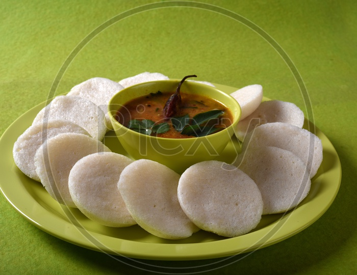 Idli with Sambar in bowl on green background, Indian Dish : south Indian favourite food rava idli or semolina idly or rava idly, served with sambar and green coconut chutney.