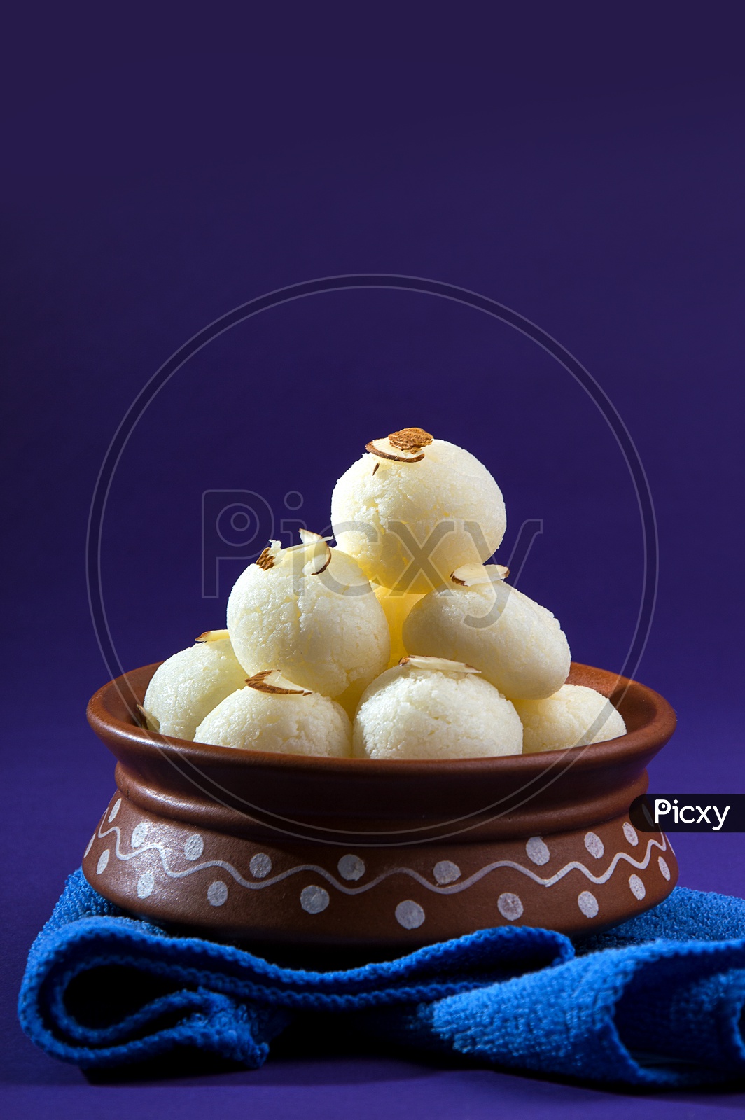 Rasgulla in a clay bowl with blue napkin on violet background