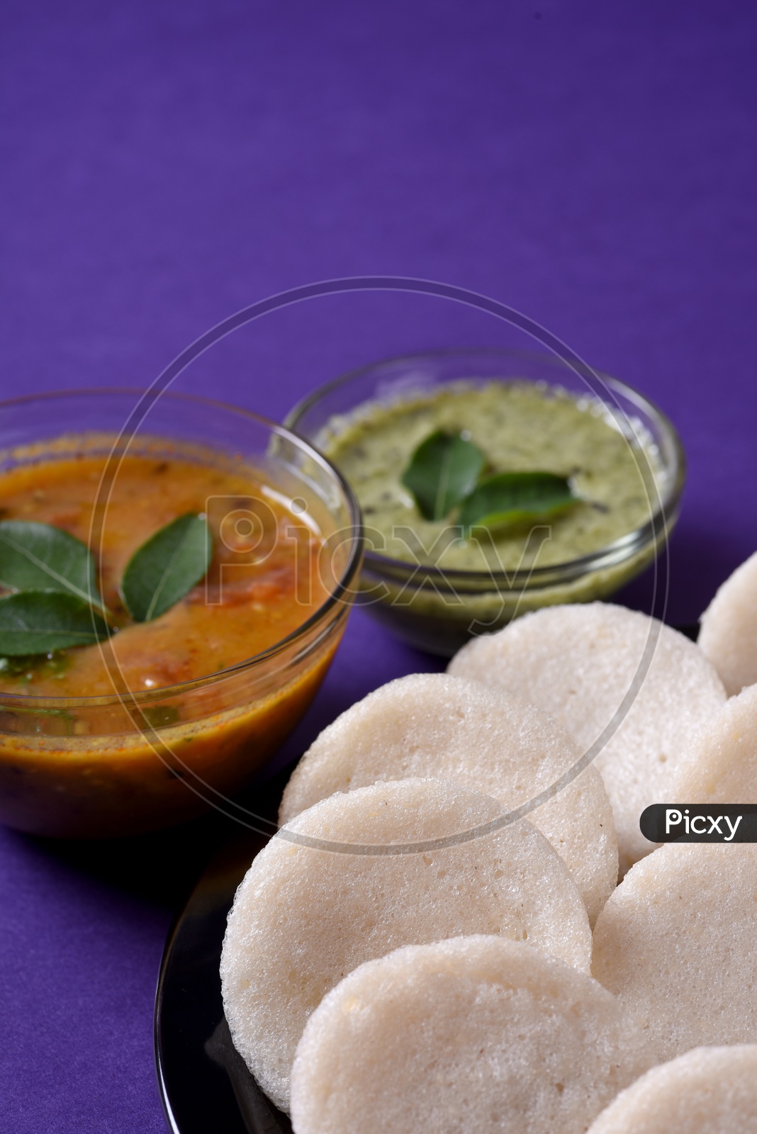 Idli served with sambar and coconut chutney on violet background