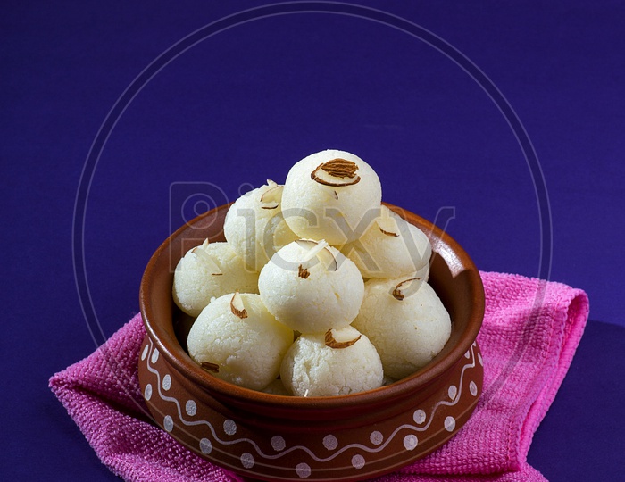 Rasgulla in a clay bowl with napkin on violet background