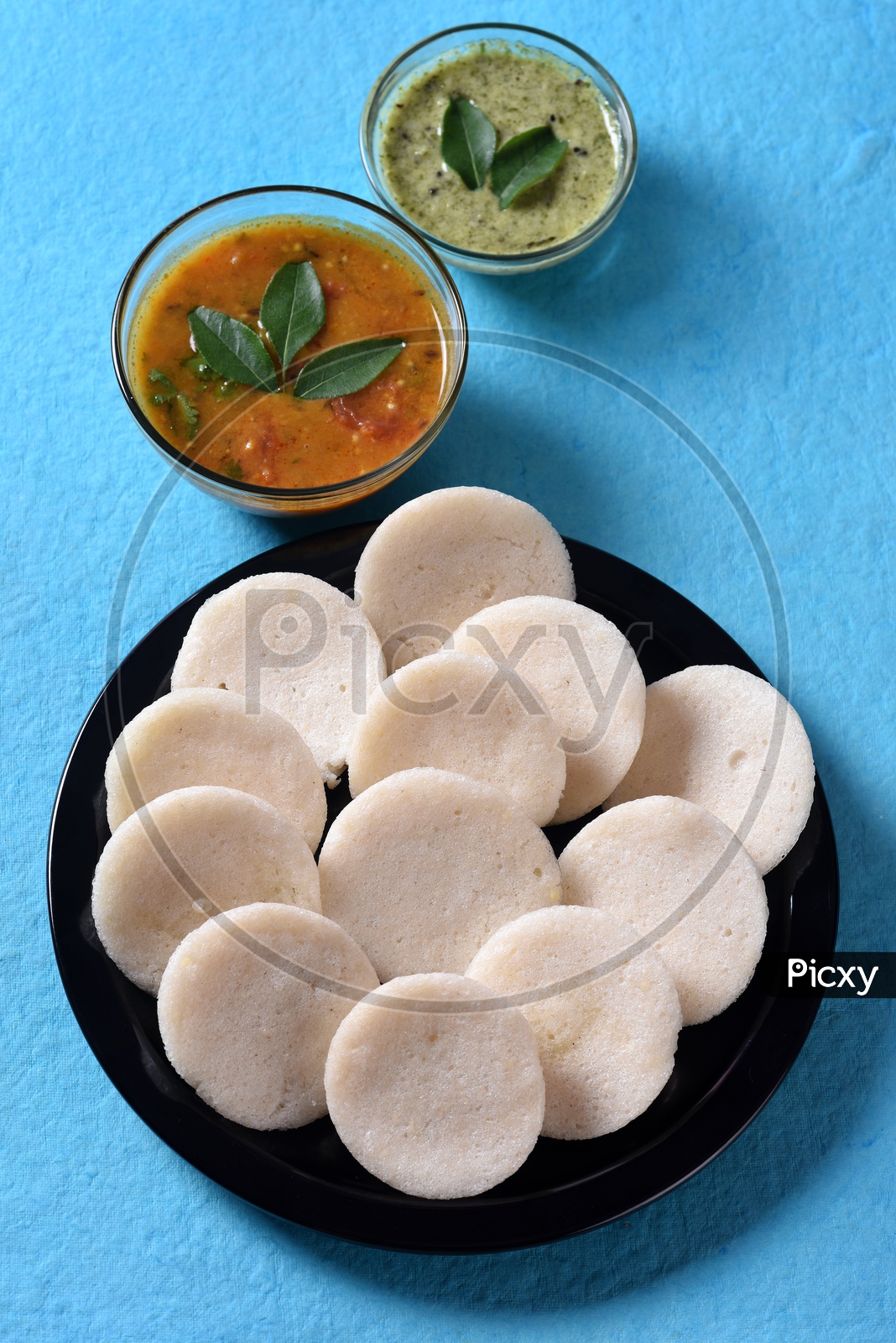 Idli served with sambar and coconut chutney on blue background
