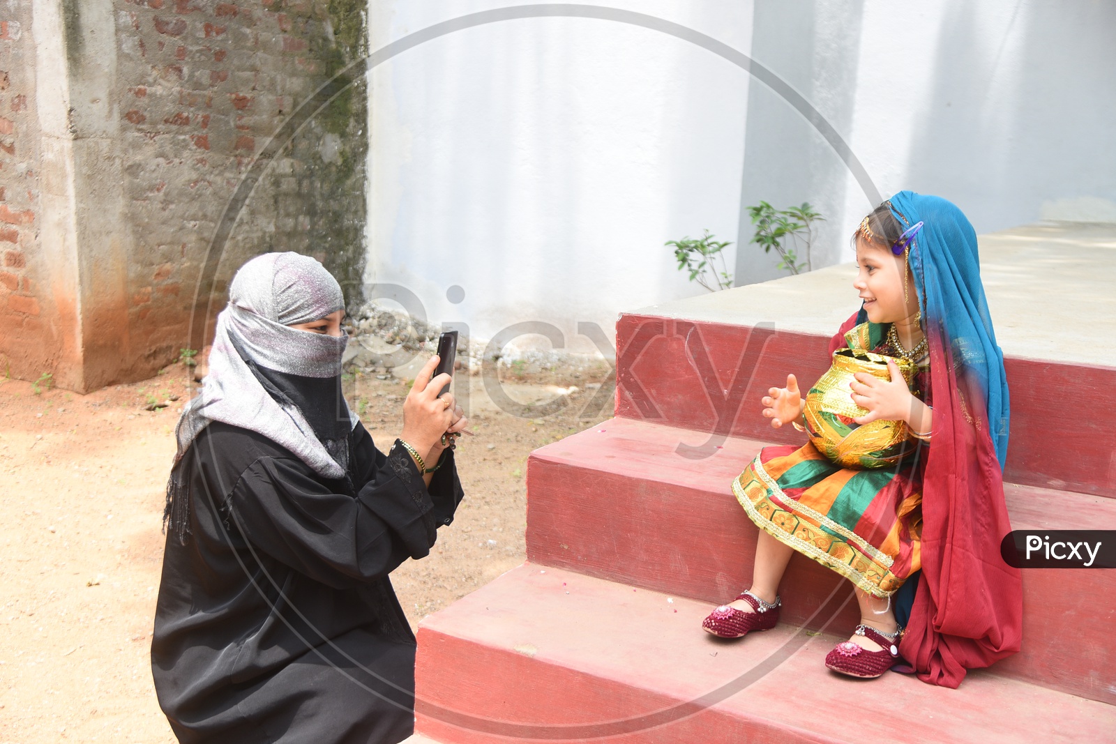Mom clicking her little girl dressed as Gopika with a decorated earthen pot