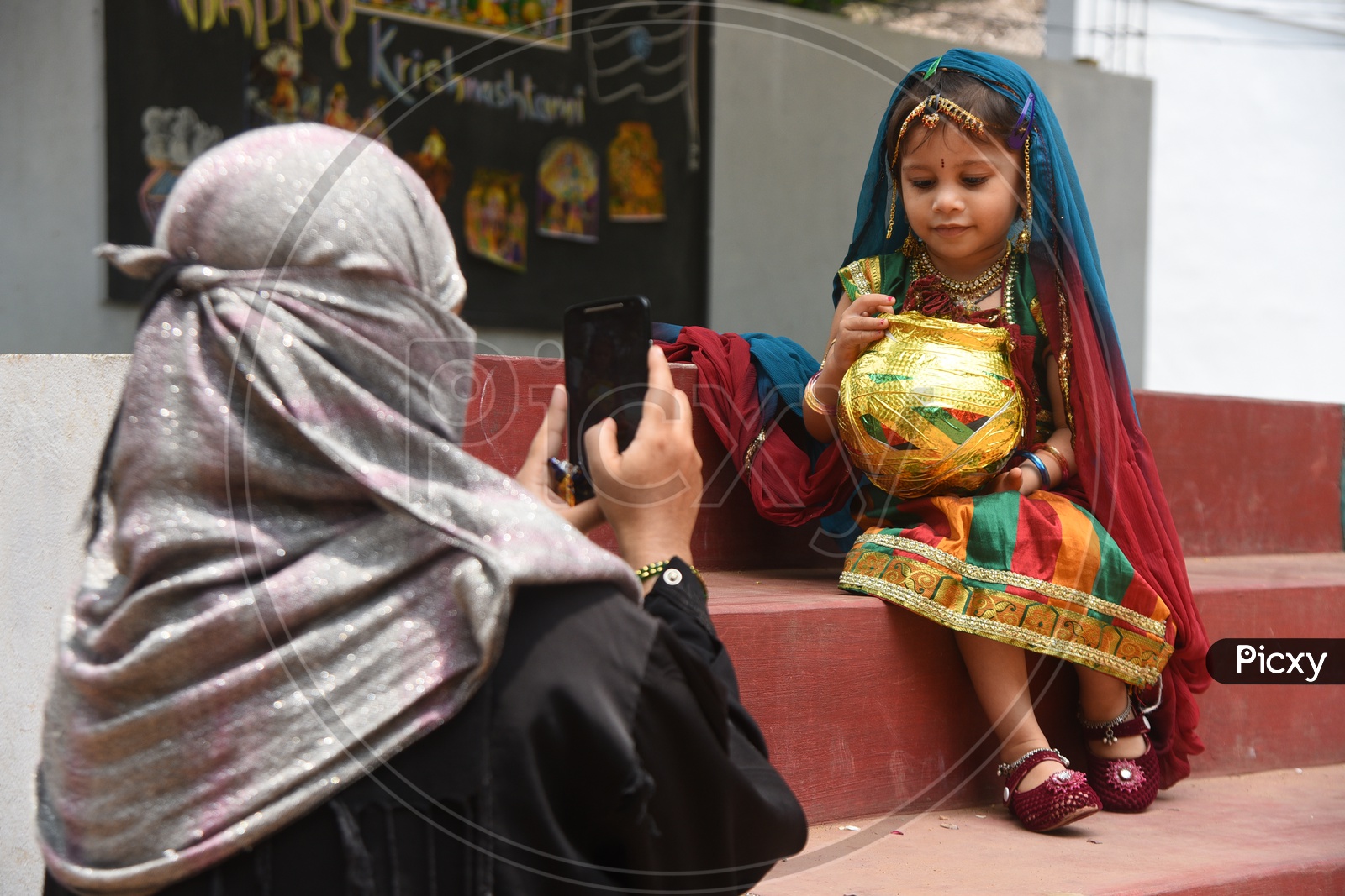 Mom clicking her little girl dressed as Gopika with a decorated earthen pot