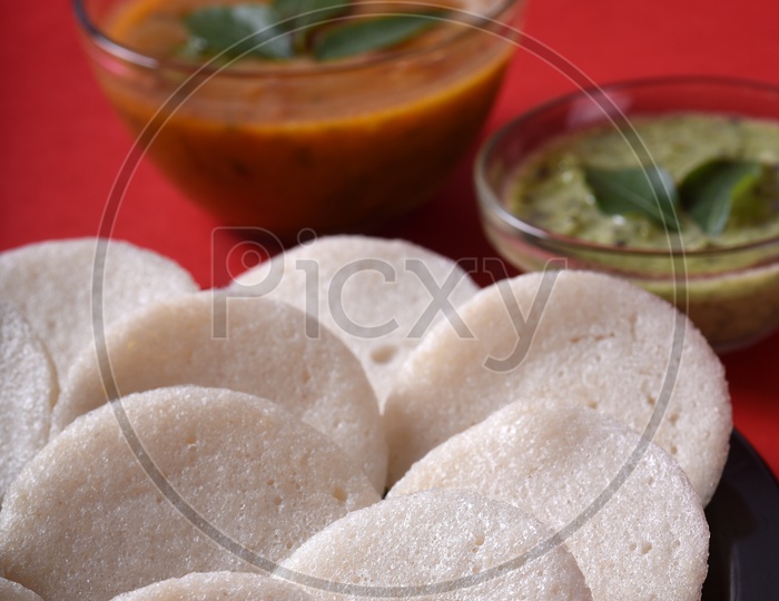 Idli with Sambar and coconut chutney on red background