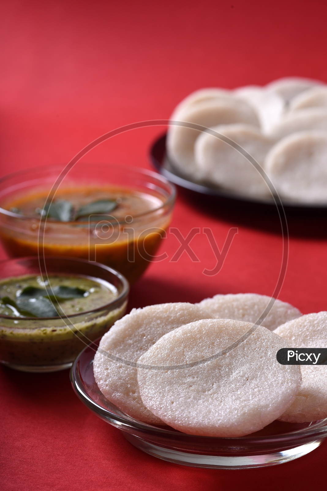 Idli served with sambar and coconut chutney on red background