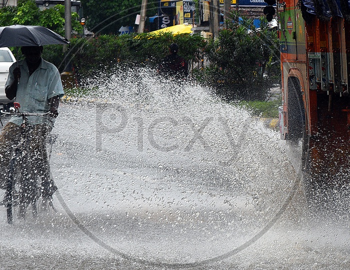 Water drops falling  onto a man who is riding a bicycle due to the moving lorry on road