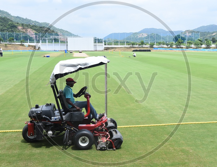 A man operating lawn mower in a cricket ground
