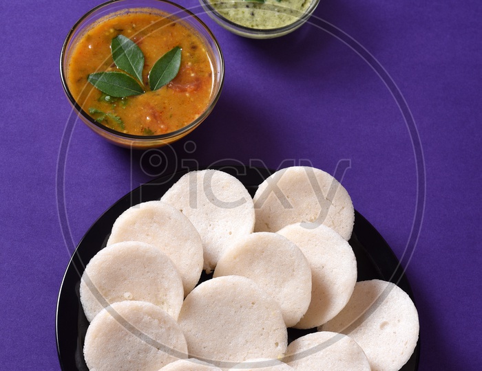 Idli served with sambar and coconut chutney on violet background