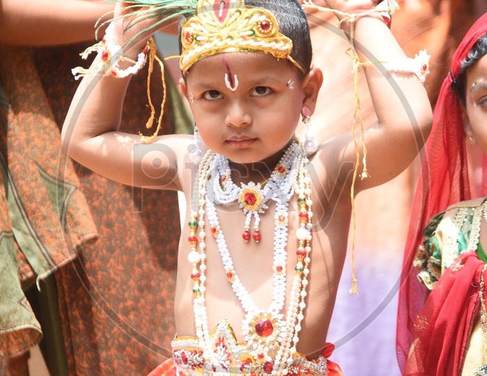 A little boy dressed as Lord Krishna with a peacock feather on his head and a flute in his hand