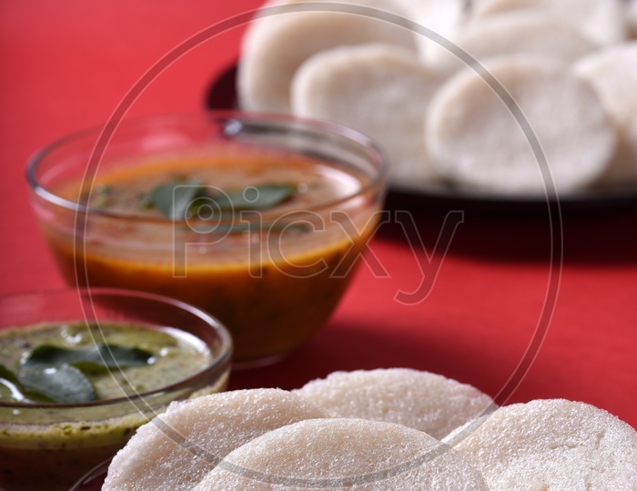 Idli served with sambar and coconut chutney on red background