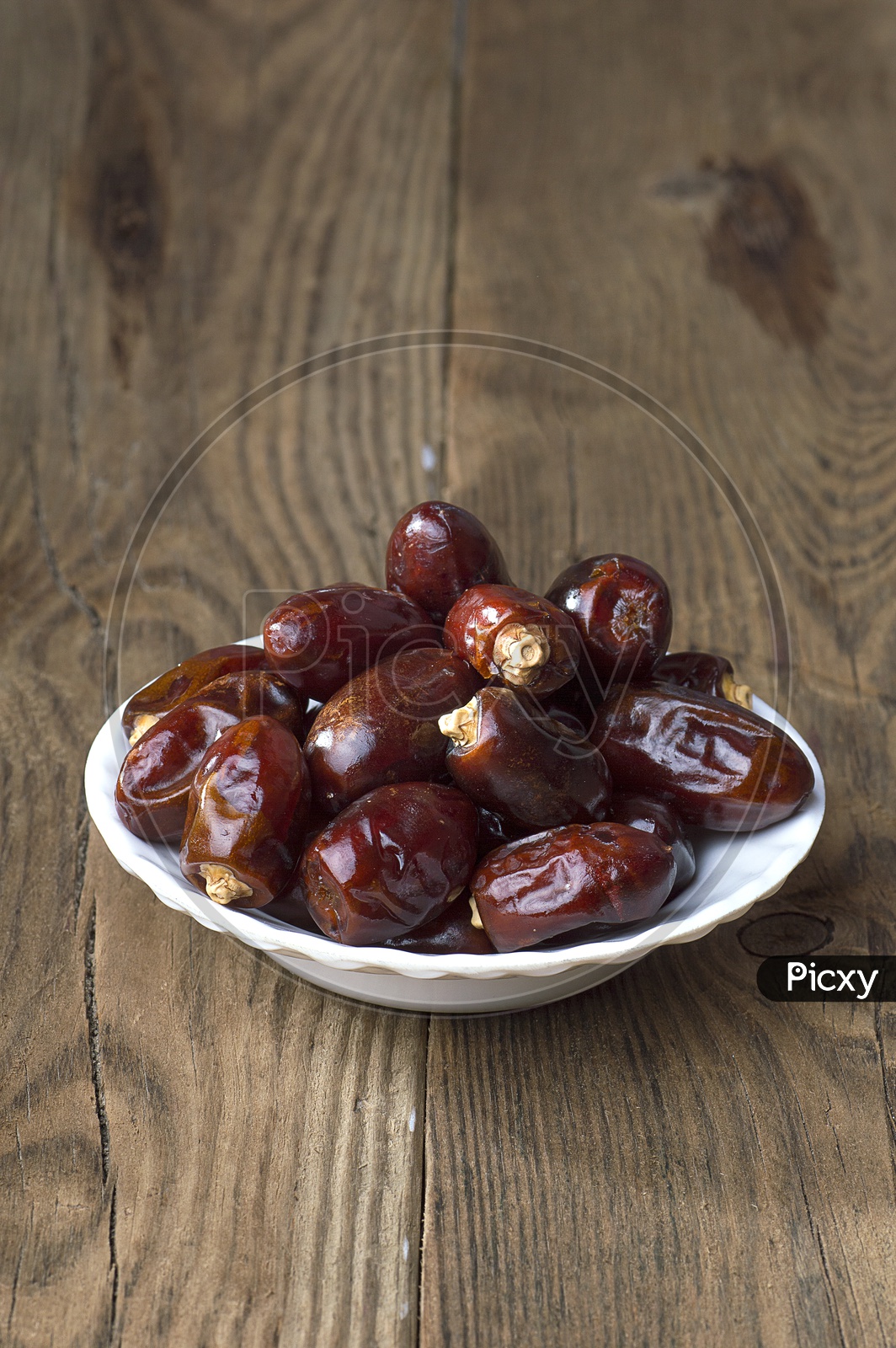Dates in a white bowl on wooden backdrop
