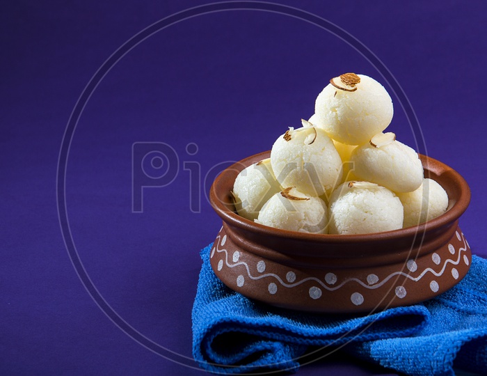 Rasgulla in a clay bowl with blue napkin on violet background