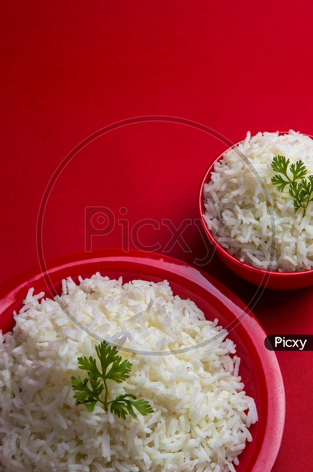 Cooked plain white basmati rice in bowl and plate on red background.