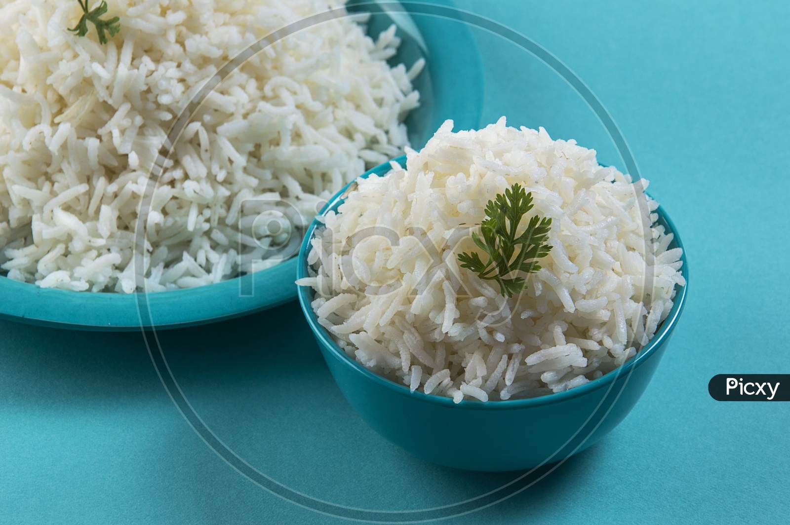Cooked plain white basmati rice in a blue plate and bowl on blue background