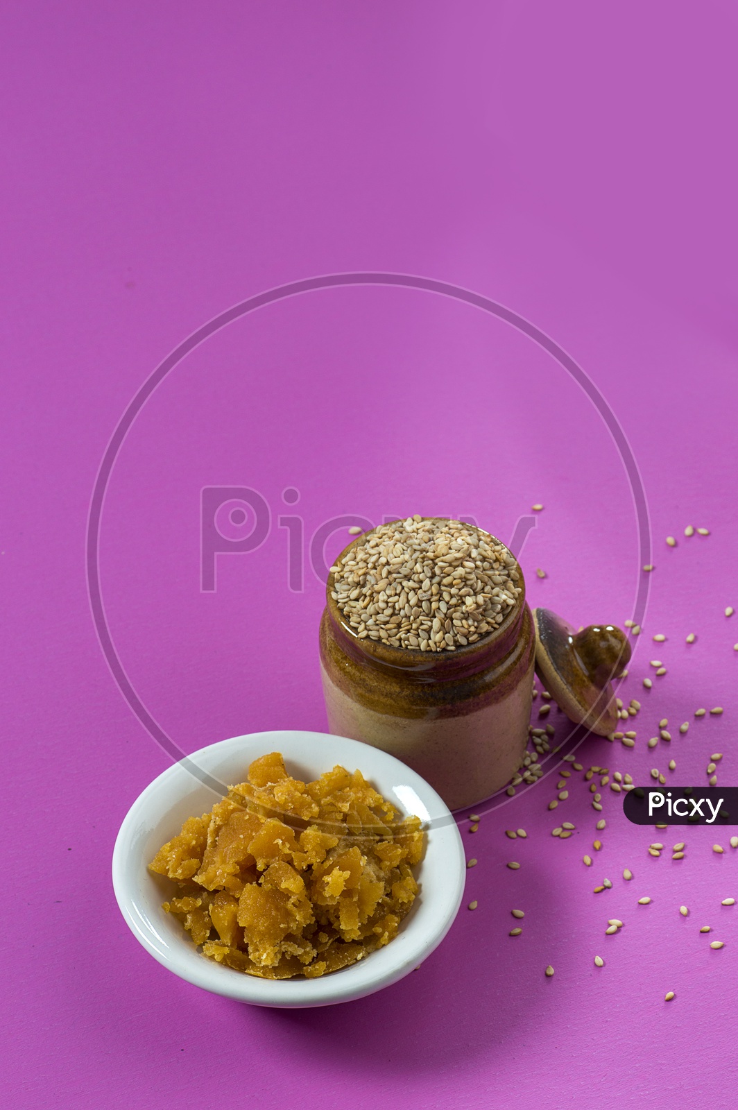 Sesame Seeds in clay pot with Jaggery in bowl on pink background