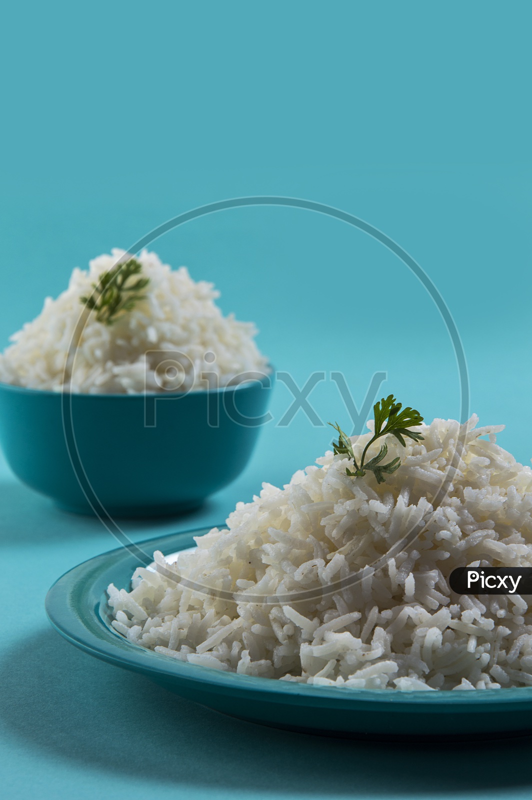 Cooked plain white basmati rice in a blue plate and bowl on blue background