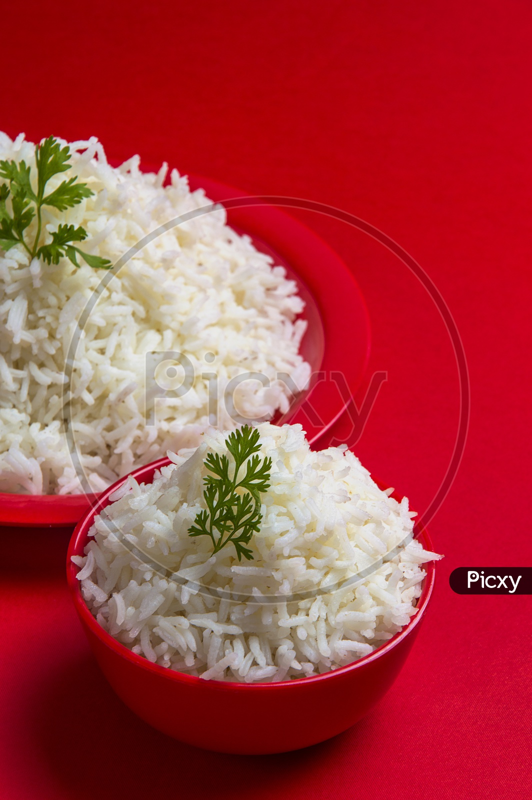 Cooked plain white basmati rice in bowl and plate on red background.