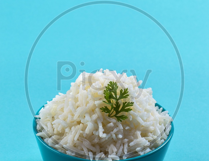 Cooked plain white basmati rice with coriander in a blue bowl on blue background