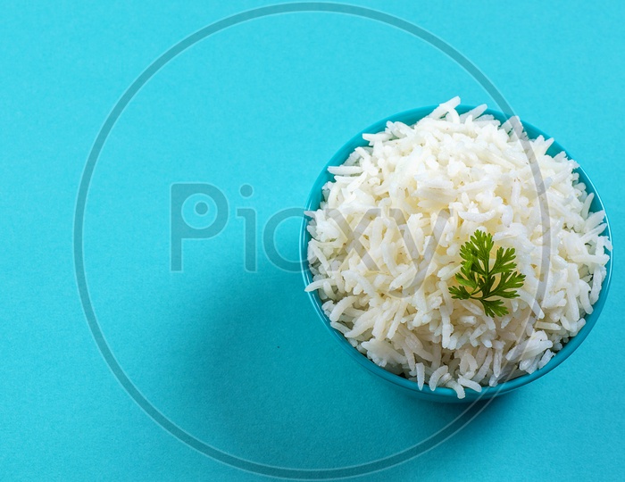 Cooked plain white basmati rice with corriander in a blue bowl on blue background