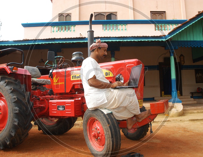 An Indian farmer using laptop sitting on a tractor