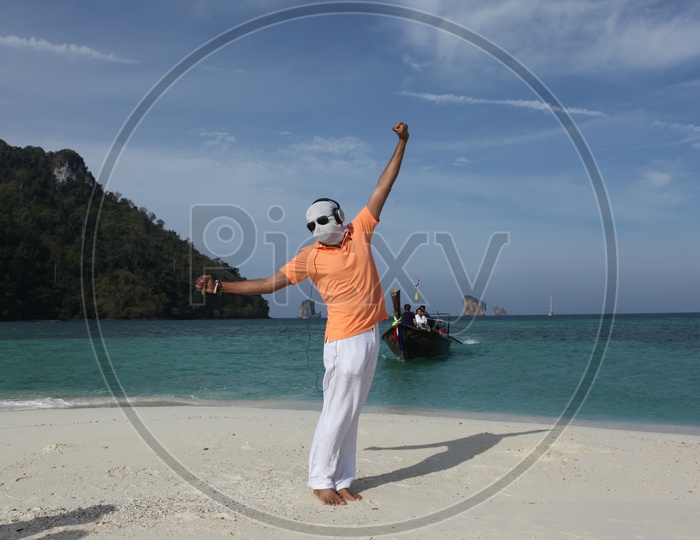 A man with white cloth face mask and goggles, dancing at the beach