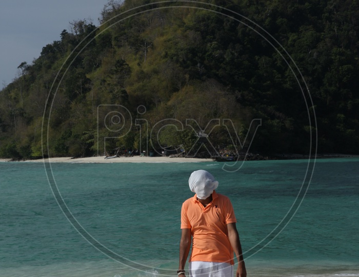 A man covered with his face cover with white cloth walking at the beach
