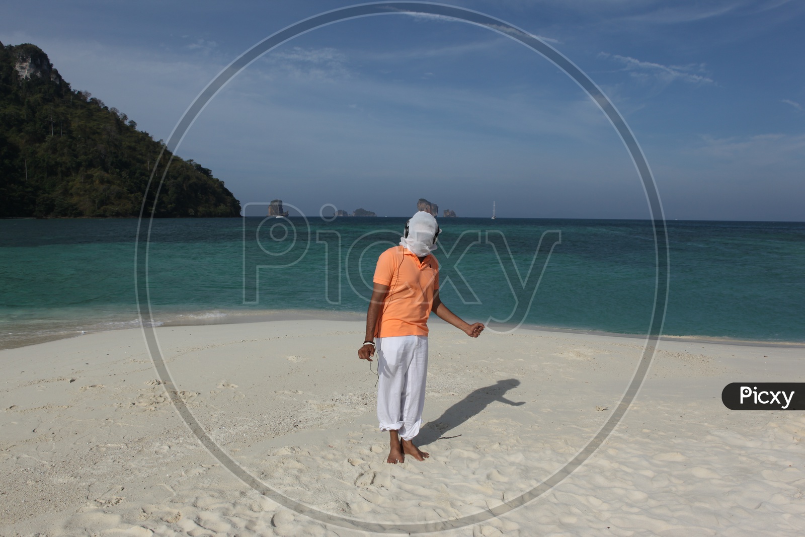 A man covered with his face cover with white cloth dancing at the beach