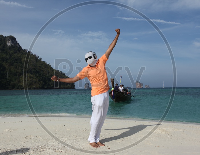 A man with white cloth face mask and goggles, dancing at the beach