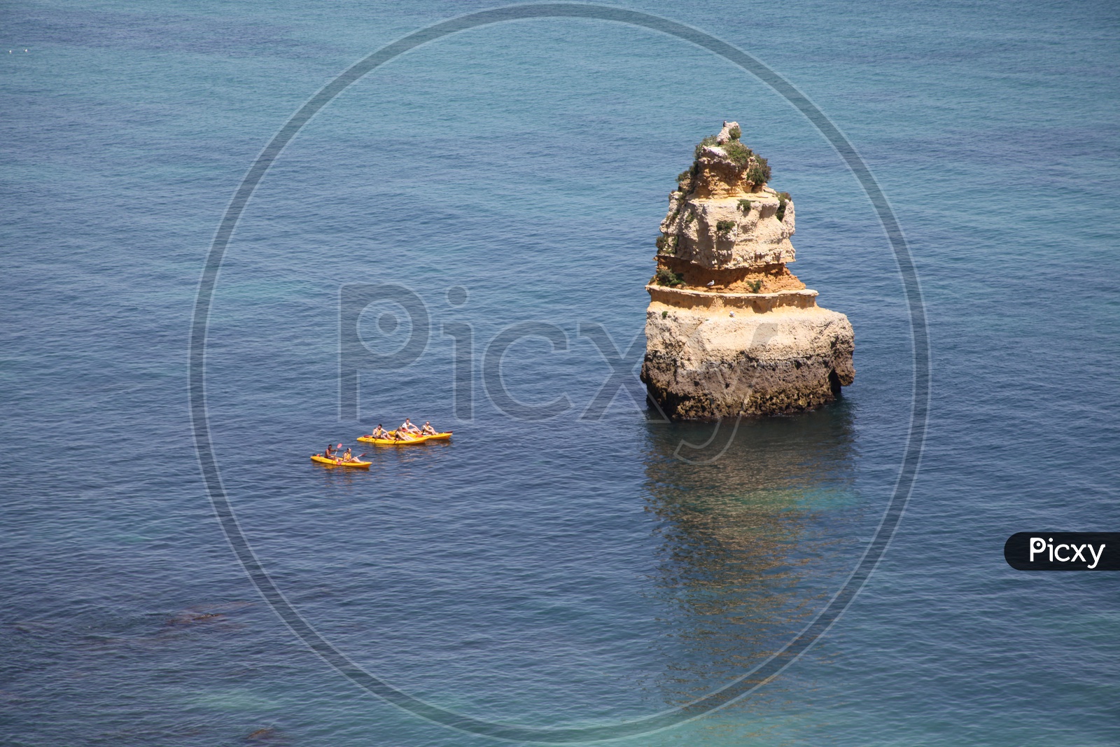 A large rock in the sea and boats passing beside it