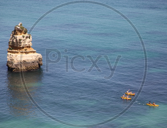 people moving in small boats on the sea and a large rock beside