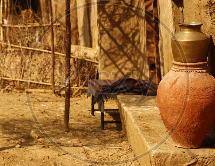 Clay pot and brass utensil in front of a mud hut