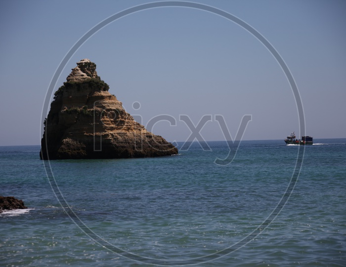a stationary large rock in the sea and a boat moving beside it