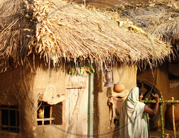 A woman standing near a thatched mud hut