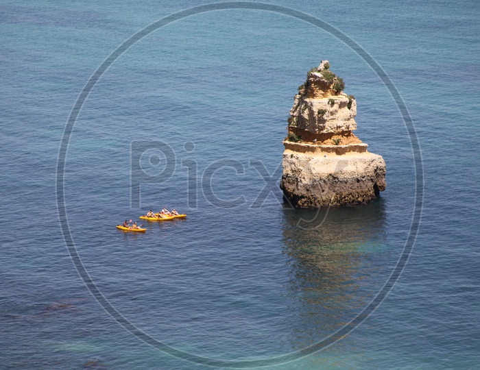 A large rock in the sea and boats passing beside it