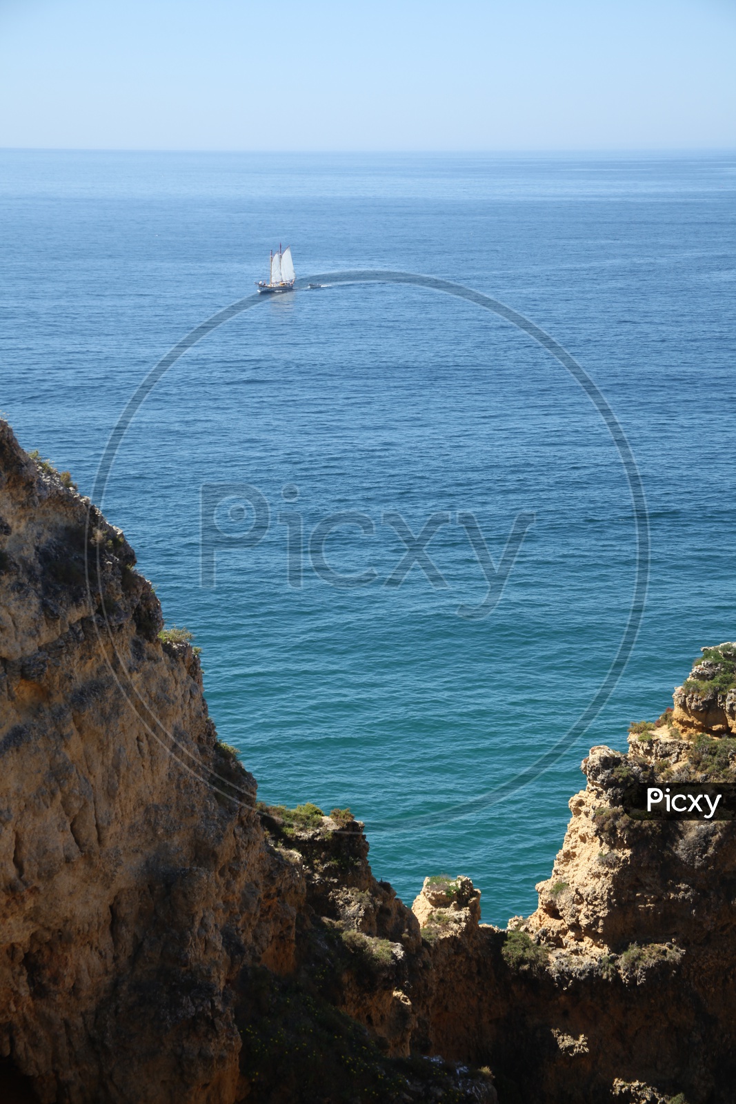 view of sail boat moving in sea from the top of a cliff
