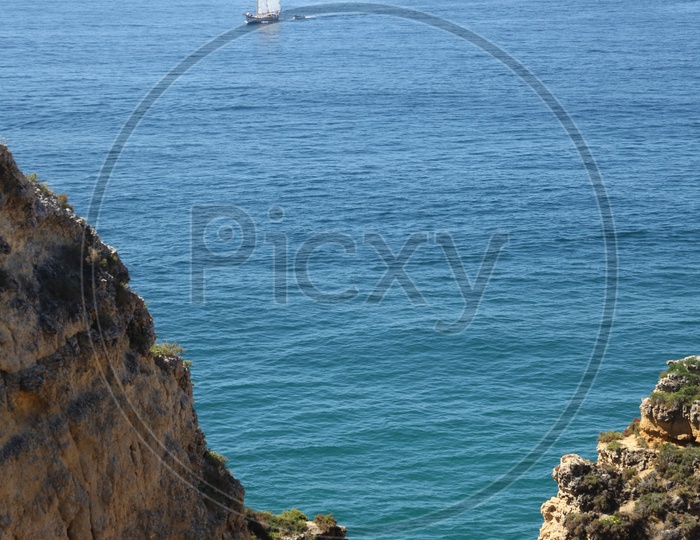 view of sail boat moving in sea from the top of a cliff