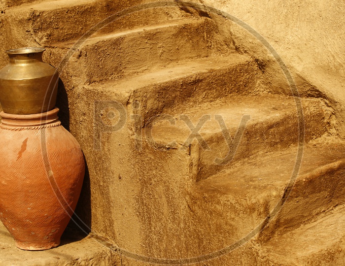 Clay pot and brass utensil near a Staircase made of mud