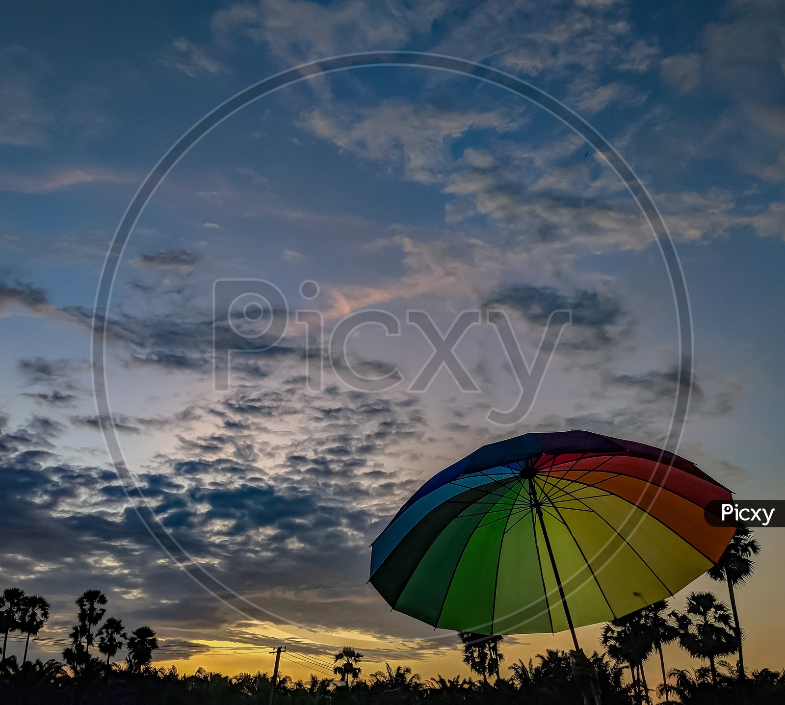 A Rainbow Coloured Umbrella over A Sunset Sky With Clouds In Background