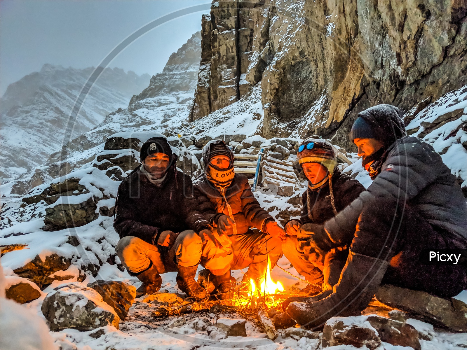 Adventurers Or Travelers at Camp Fire At Snow Capped Mountains