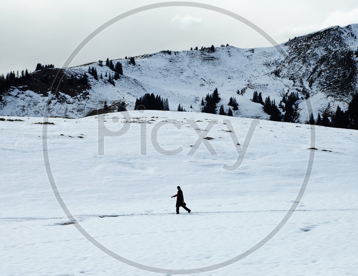 A Man Walking Alone in Snow Capped Mountains