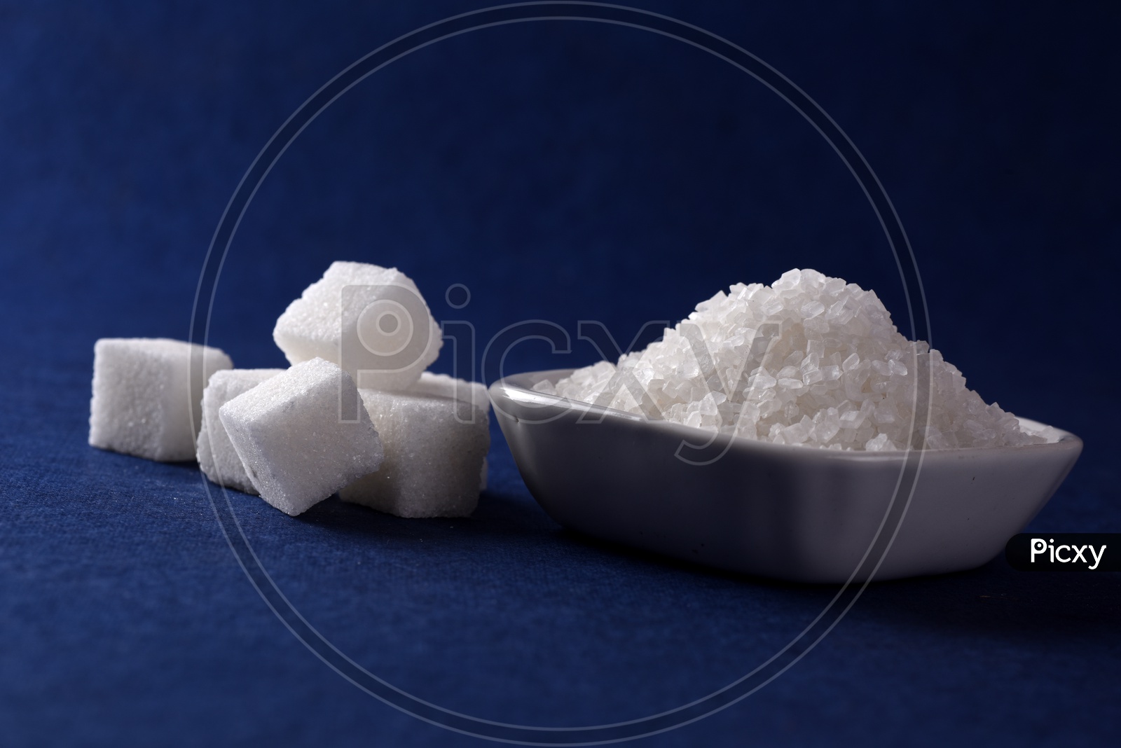 Sugar cubes and granulated sugar in a ceramic plate on blue background