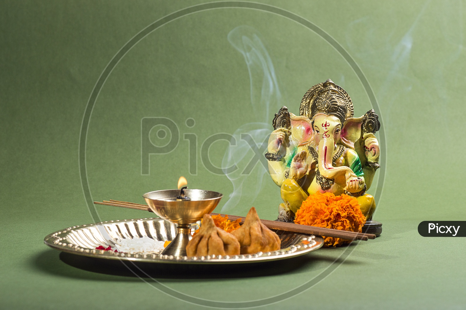Lord Ganesh Idol with flowers and lightened up diya on green background