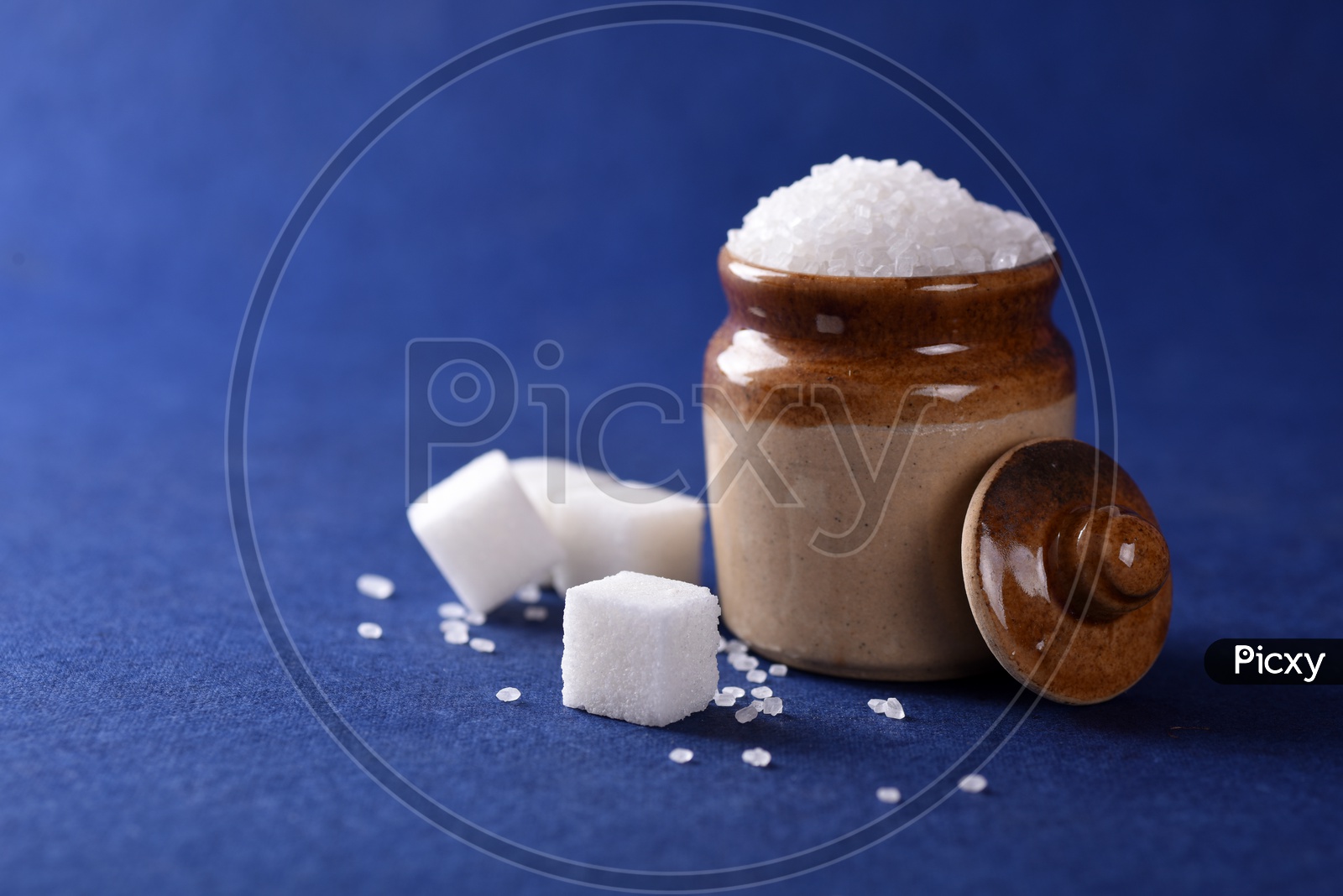 Sugar cubes and granulated sugar in a ceramic jar on blue background