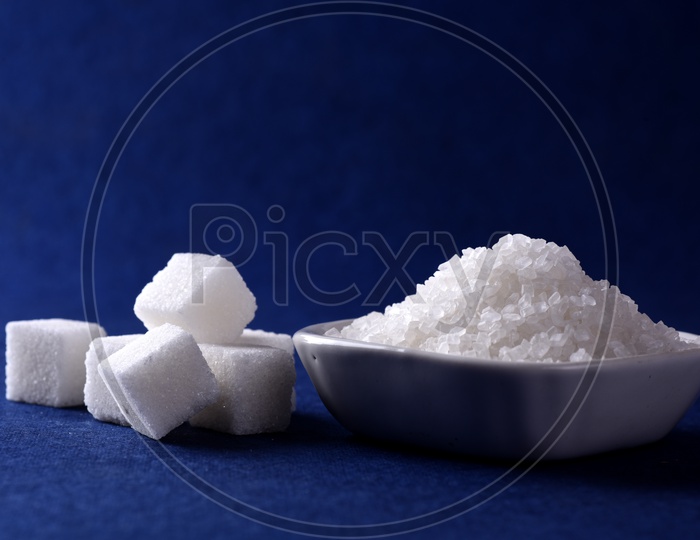 Sugar cubes and granulated sugar in a ceramic plate on blue background