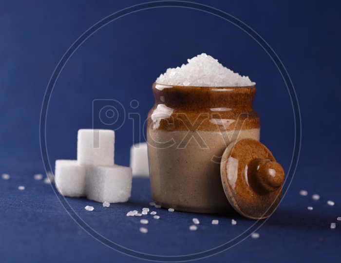 Sugar cubes and granulated sugar in a ceramic jar on dark blue background
