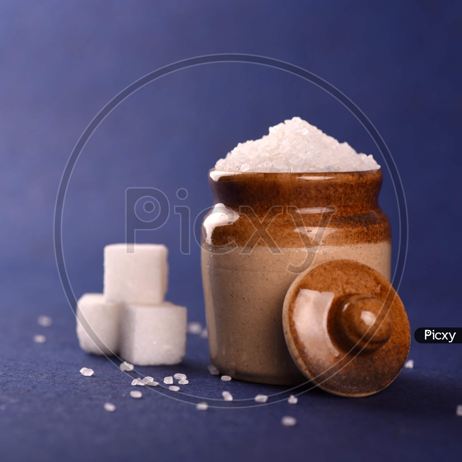 Sugar cubes and granulated sugar in a ceramic jar on blue background