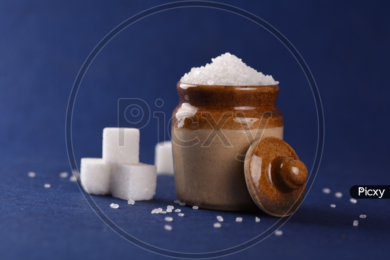 Sugar cubes and granulated sugar in a ceramic jar on dark blue background