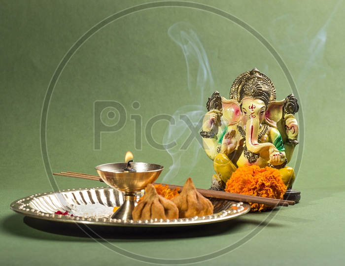 Lord Ganesh Idol with flowers and lightened up diya on green background