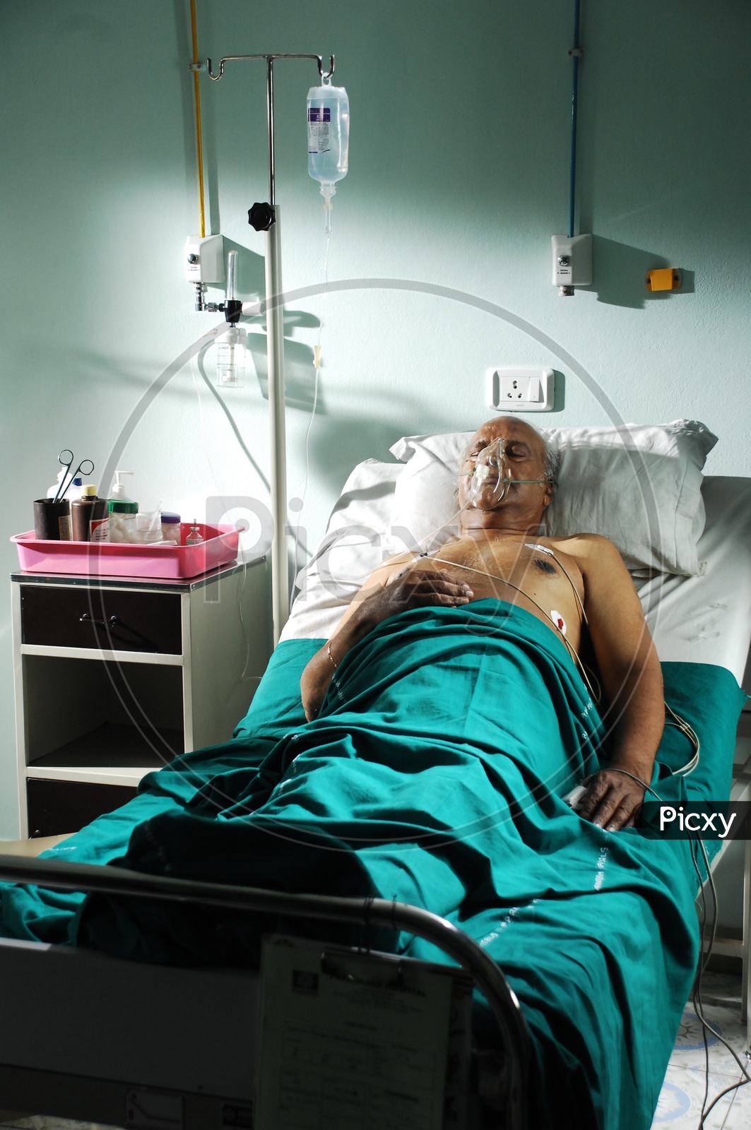 An old man in a hospital bed with oxygen mask and saline