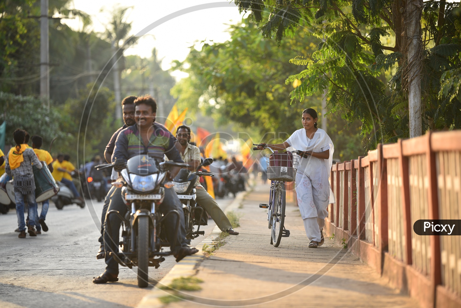 A woman walking on the footpath along with a bicycle as the TDP party supporters were riding bikes on the road during an election campaign rally